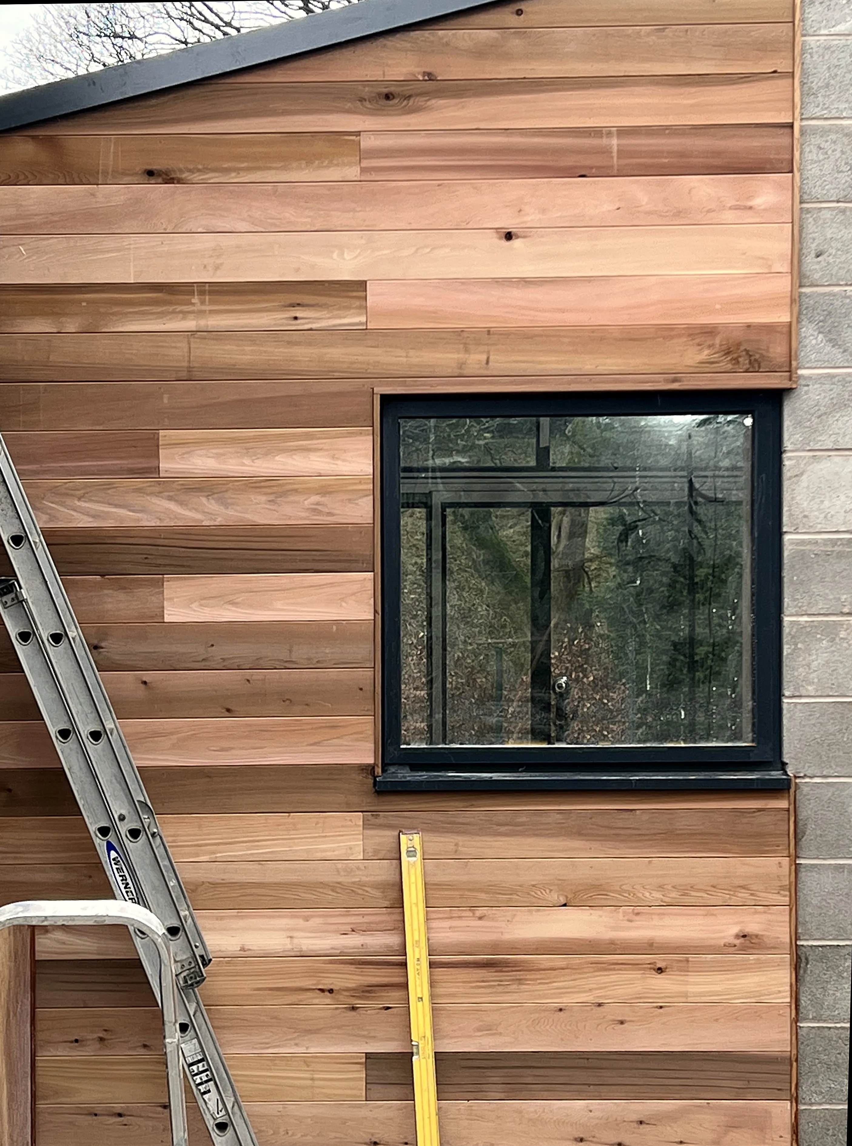 Cedar cladding being fixed to a new extension, with a ladder and spirit level against the boards